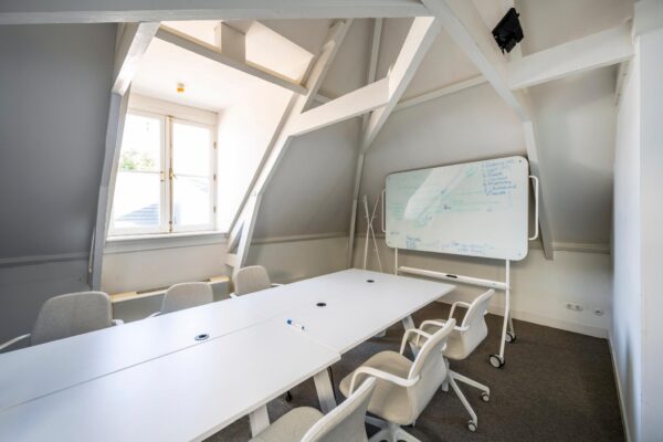 Vergaderruimte aan de Prof. Tulpstraat met een schuine kap, witte vergadertafel, comfortabele stoelen en een whiteboard.